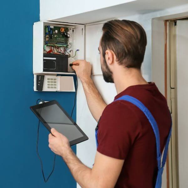 Home Security Guys carrying out home alarm repair Brisbane with open alarm control box and internal wiring inspection.